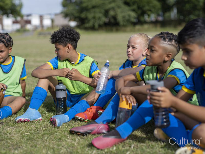 Children dressed in uniforms sitting on soccer field
