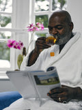 Mature man in white bathrobe reading magazine and drinking tea