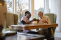 Smiling senior man and nurse playing cards at table in nursing home