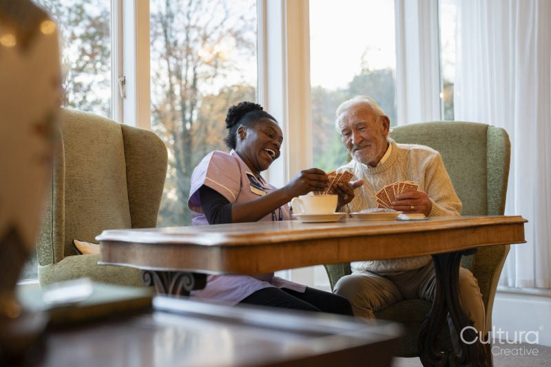 Smiling senior man and nurse playing cards at table in nursing home