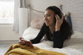 Teenage girl listening music on smart phone while lying on bed at home