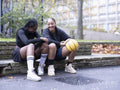 Two female friends sitting outdoors with basketball