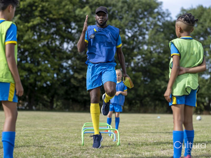 Kids watching coach perform warming-up exercises on soccer field