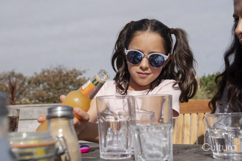 Girl pouring orange juice into drinking glass in outdoor restaurant