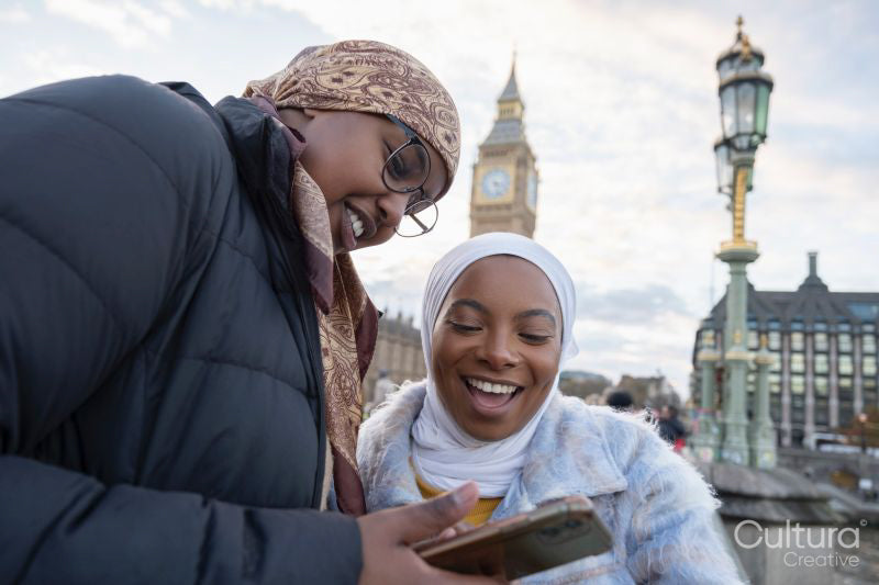Young female tourists in hijabs using phone on Westminster Bridge