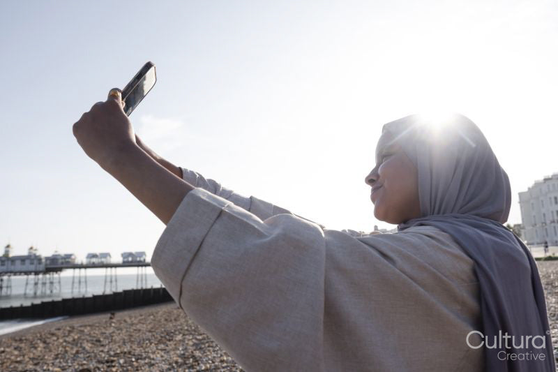 Muslim woman taking selfie by sea on sunny day