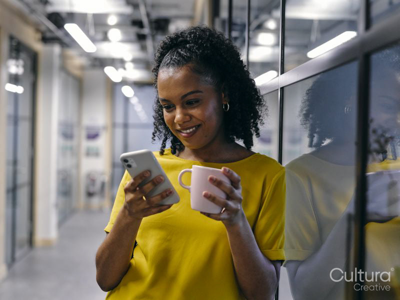 Woman drinking coffee and using phone in office hallway