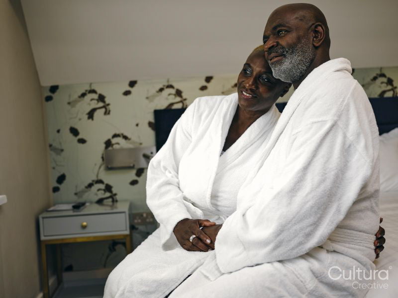 Mature couple in bathrobes sitting on bed in hotel room