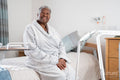 Smiling senior woman in bathrobe sitting on bed in nursing home