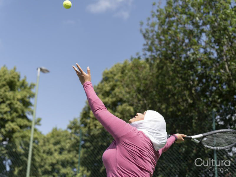 Sutton,Woman in headscarf playing tennis in park