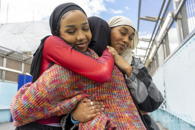 Young women wearing hijabs hugging in city