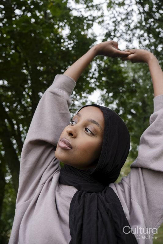 Portrait of woman in hijab stretching in park