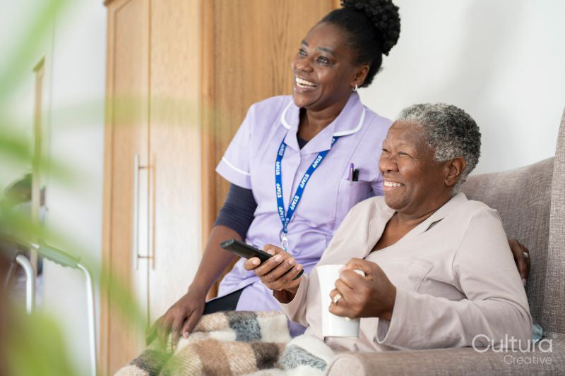Caregiver and senior woman watching TV and laughing