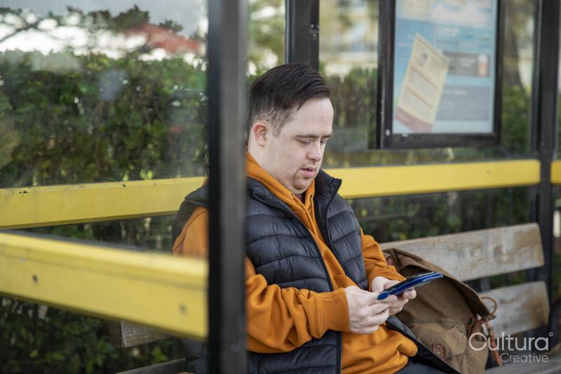 Man sitting on bench at bus stop, using smart phone