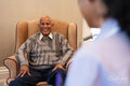 Smiling senior man sitting in armchair and looking at nurse