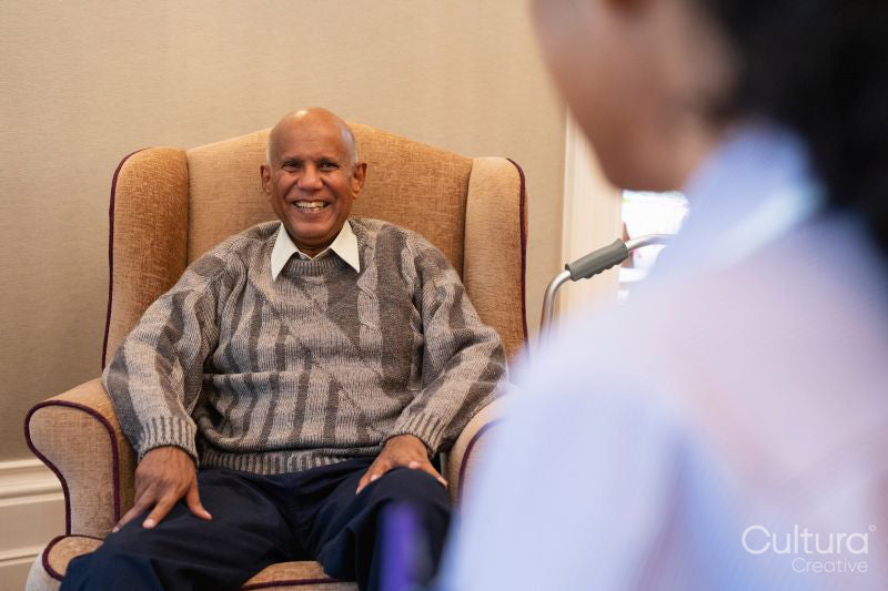 Smiling senior man sitting in armchair and looking at nurse