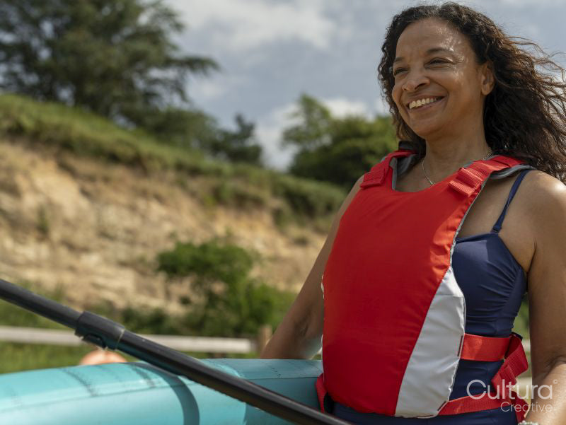 Portrait of smiling woman carrying paddleboard and oar on beach