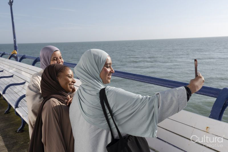 Three Muslim women taking selfie while standing on pier on sunny day