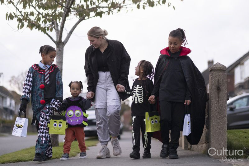 Woman with children in Halloween costumes walking on sidewalk