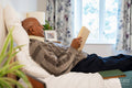 Senior man reading book while lying on bed in his room at nursing home