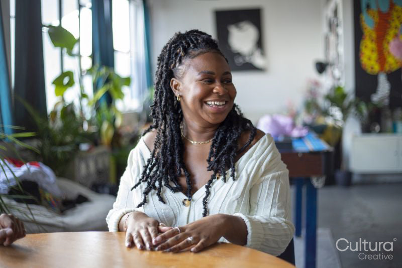 Smiling woman with black dreadlocks sitting at table during card game