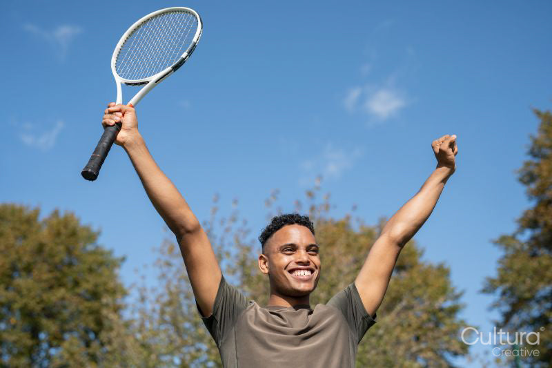 Smiling man raising arms with tennis racket