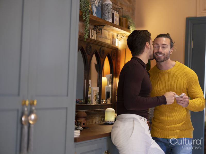 man kissing boyfriend while holding ultrasound scan at home