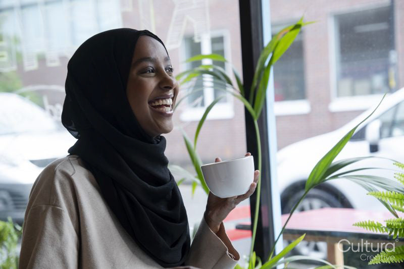 Smiling young woman in hijab drinking coffee in cafe