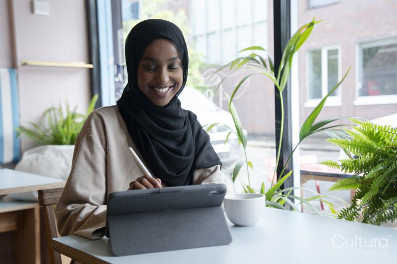Young woman in hijab working on tablet in cafe