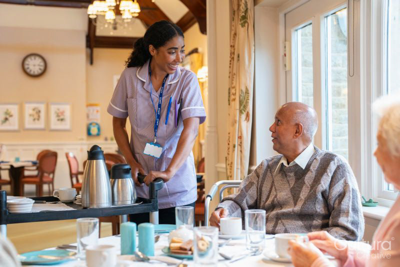 Dietitian serving coffee to group of seniors at cafeteria in nursing home