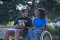 Teenage girl in wheelchair with friend relaxing in park