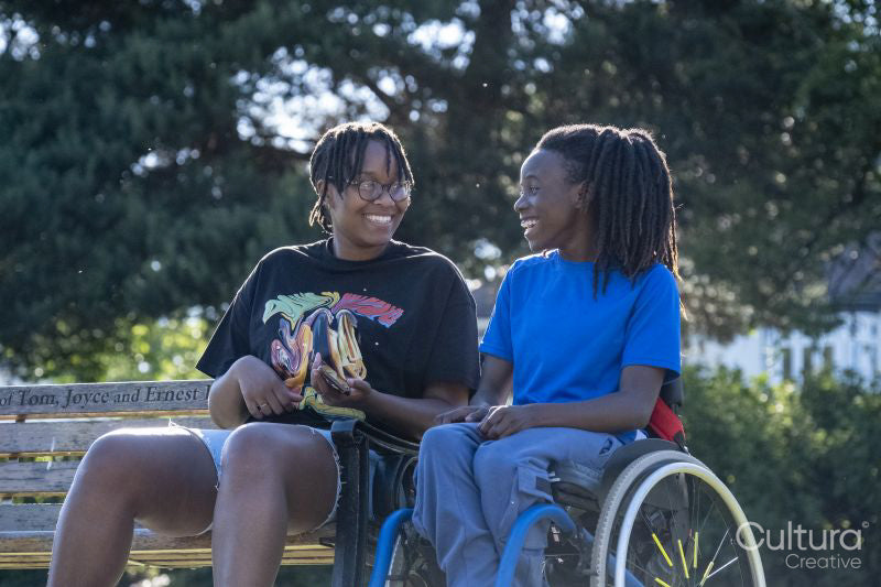 Teenage girl in wheelchair with friend relaxing in park