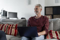 Smiling mature man working on laptop on sofa at home