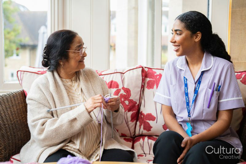 Senior woman knitting and talking to care giver in nursing home