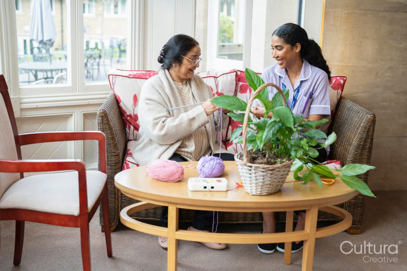 Senior woman knitting and talking to care giver in nursing home