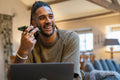 Man with dreads talking on phone and working on laptop at home