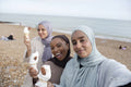 Portrait of three Muslim women standing with ice creams on beach