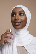 Studio shot of smiling young woman in white hijab using perfume