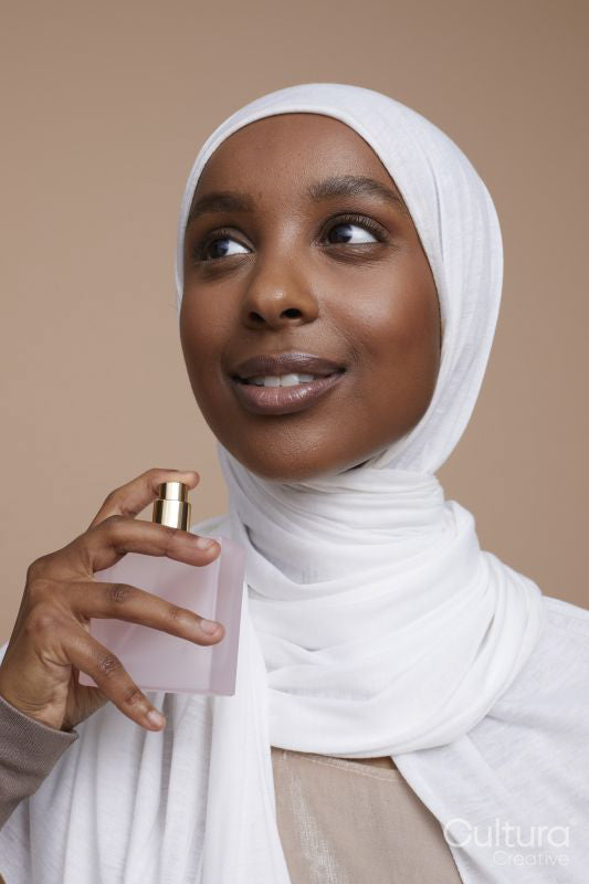 Studio shot of smiling young woman in white hijab using perfume