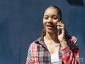 Young woman talking by smart phone against blue wall