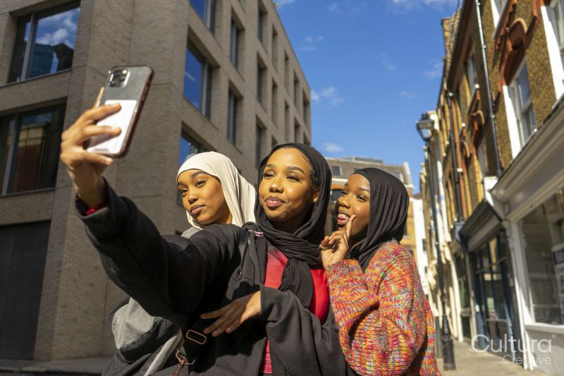 Smiling young women wearing hijabs taking selfie in city