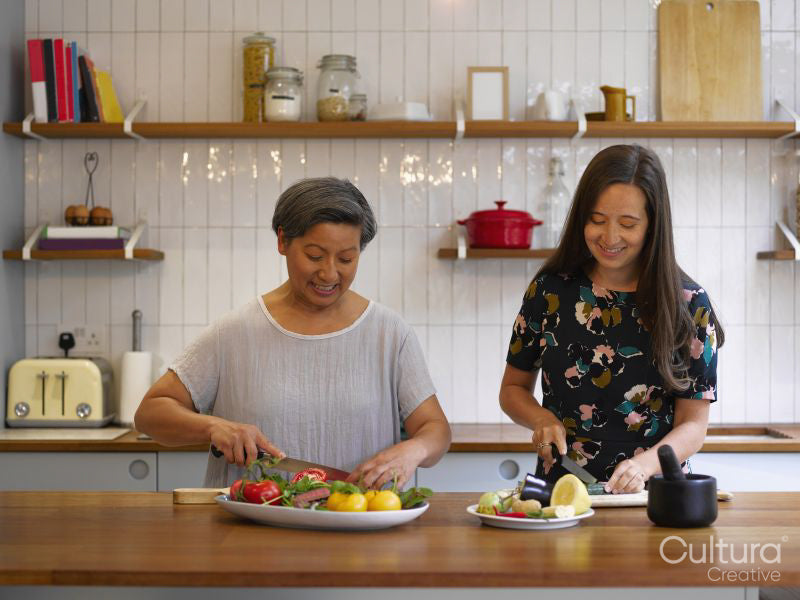 Mother and adult daughter cutting vegetables in kitchen