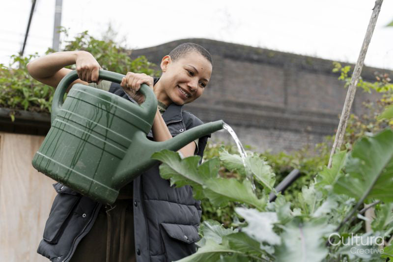 Smiling woman watering homegrown vegetables in urban garden