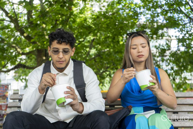 Tourist couple sitting on park bench eating street food