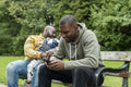 Two smiling men with daughter sitting on bench in park