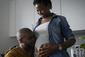 Man kissing pregnant woman's belly in kitchen