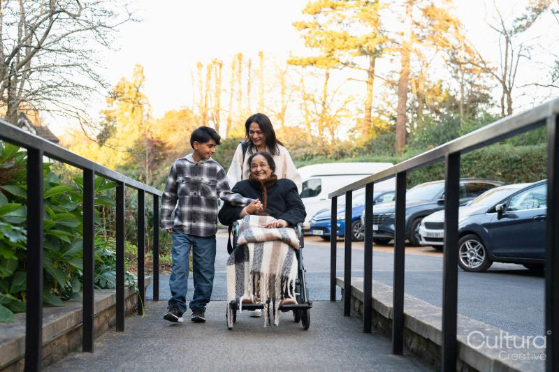 Family during walk outside nursing home with senior lady sitting in wheelchair