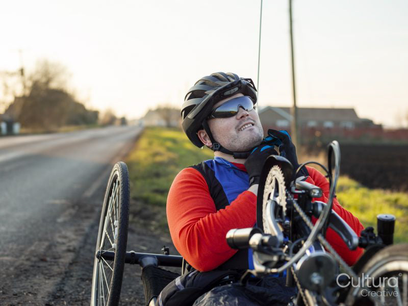 Disabled man on handcycle fastening cycling helmet on roadside
