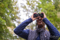 Smiling man using binoculars in forest