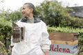 Smiling female beekeeper holding smoker in urban garden